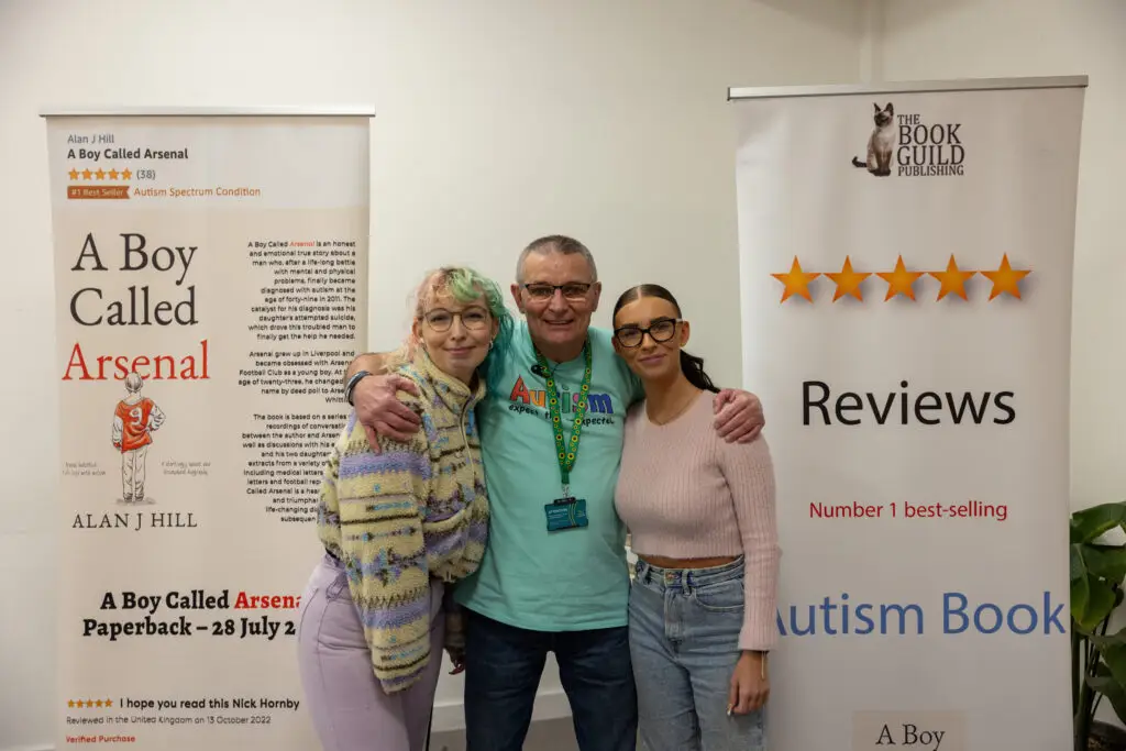 Autism activist Arsenal Whittick stands with his arms around his two daughers. In background there are banners advertising his biography, A Boy Called Arsenal, saying 'Number one best-selling autism book' and Amazon's number one bestseller for the Autism Spectrum Condition category.