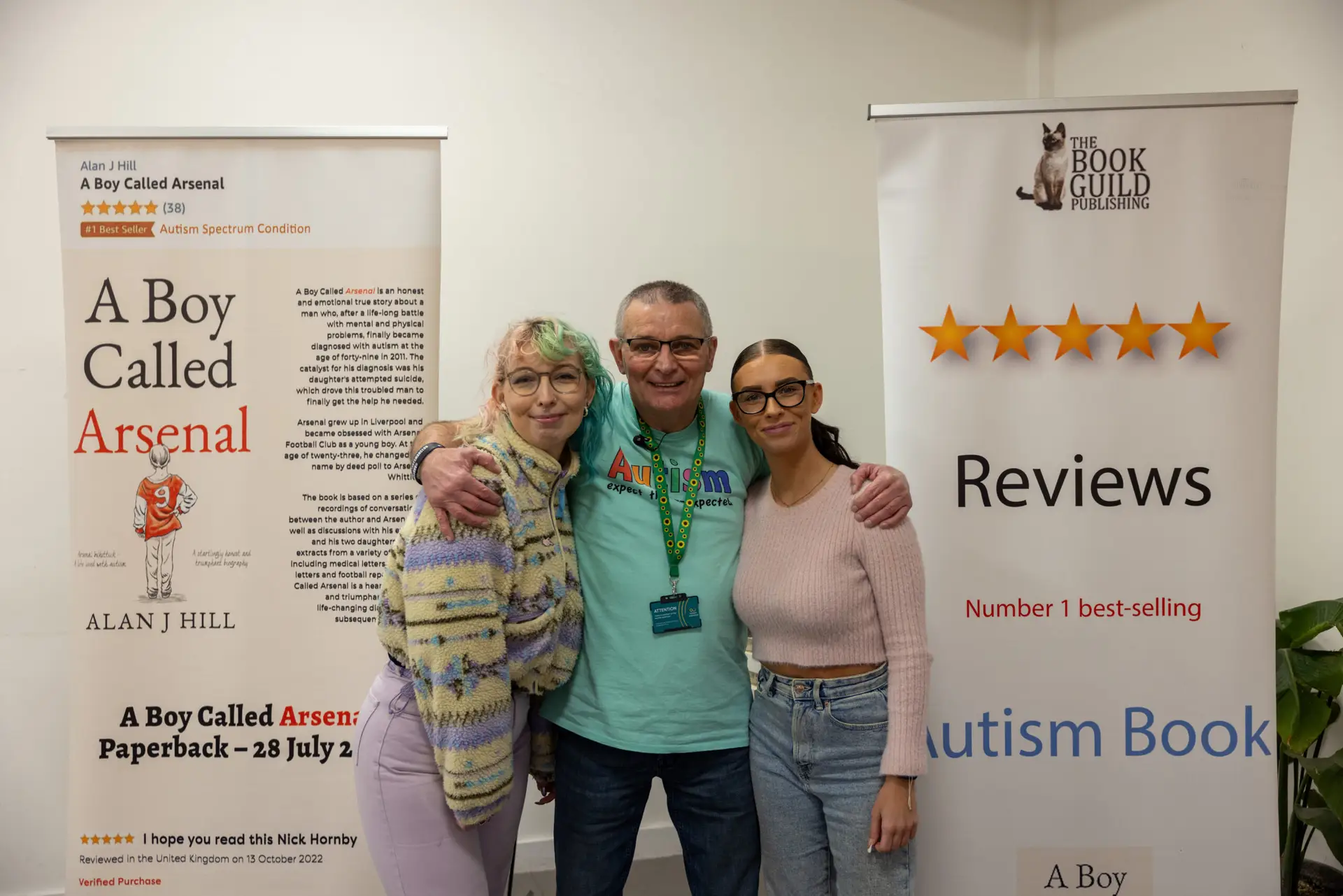 Autism activist Arsenal Whittick stands with his arms around his two daughers. In background there are banners advertising his biography, A Boy Called Arsenal, saying 'Number one best-selling autism book' and Amazon's number one bestseller for the Autism Spectrum Condition category.