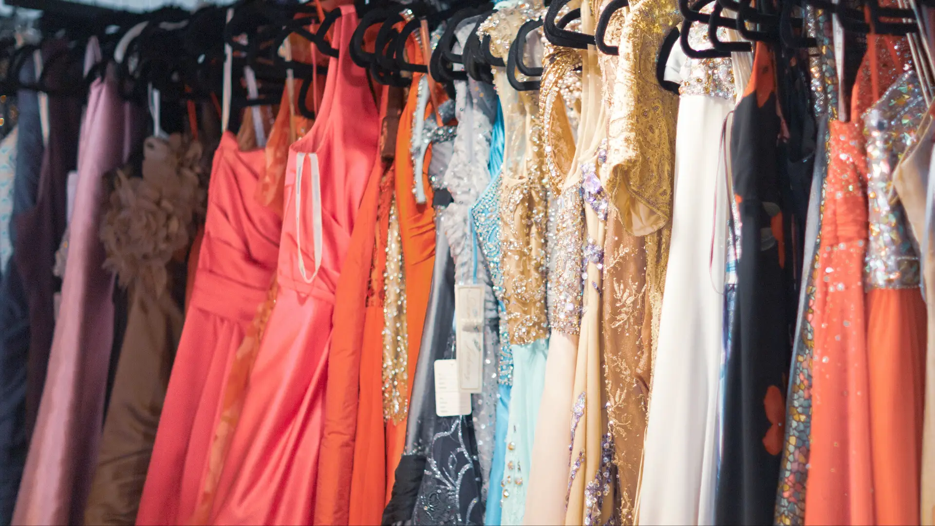A selection of prom dresses of various colours and styles hanging on a clothing rack.