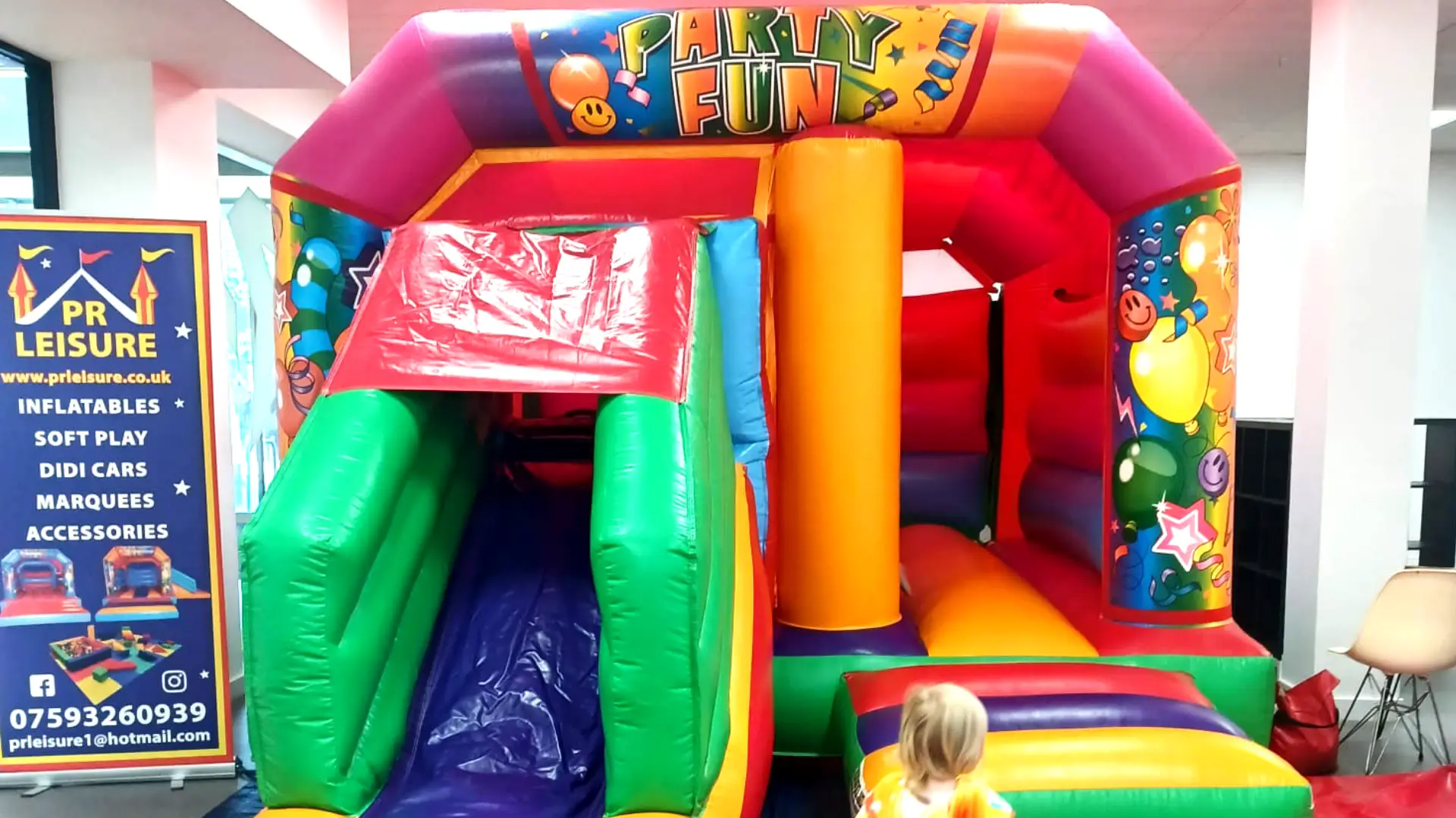 A colourful bouncy inside the Gather community events space at The Dolphin Poole. To the left of the bouncy castle is a dark blue roller banner advertising the bouncy castle hire services of PR Leisure.