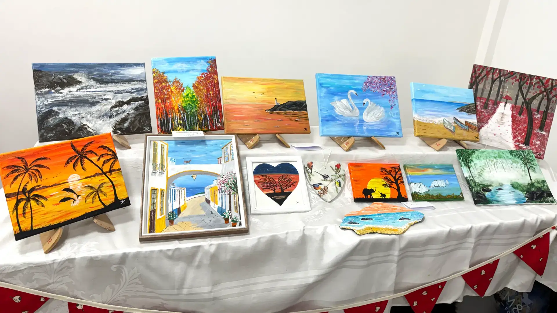 A selection of small canvases with colourful paintings of wildlife and landscapes on a tabletop.