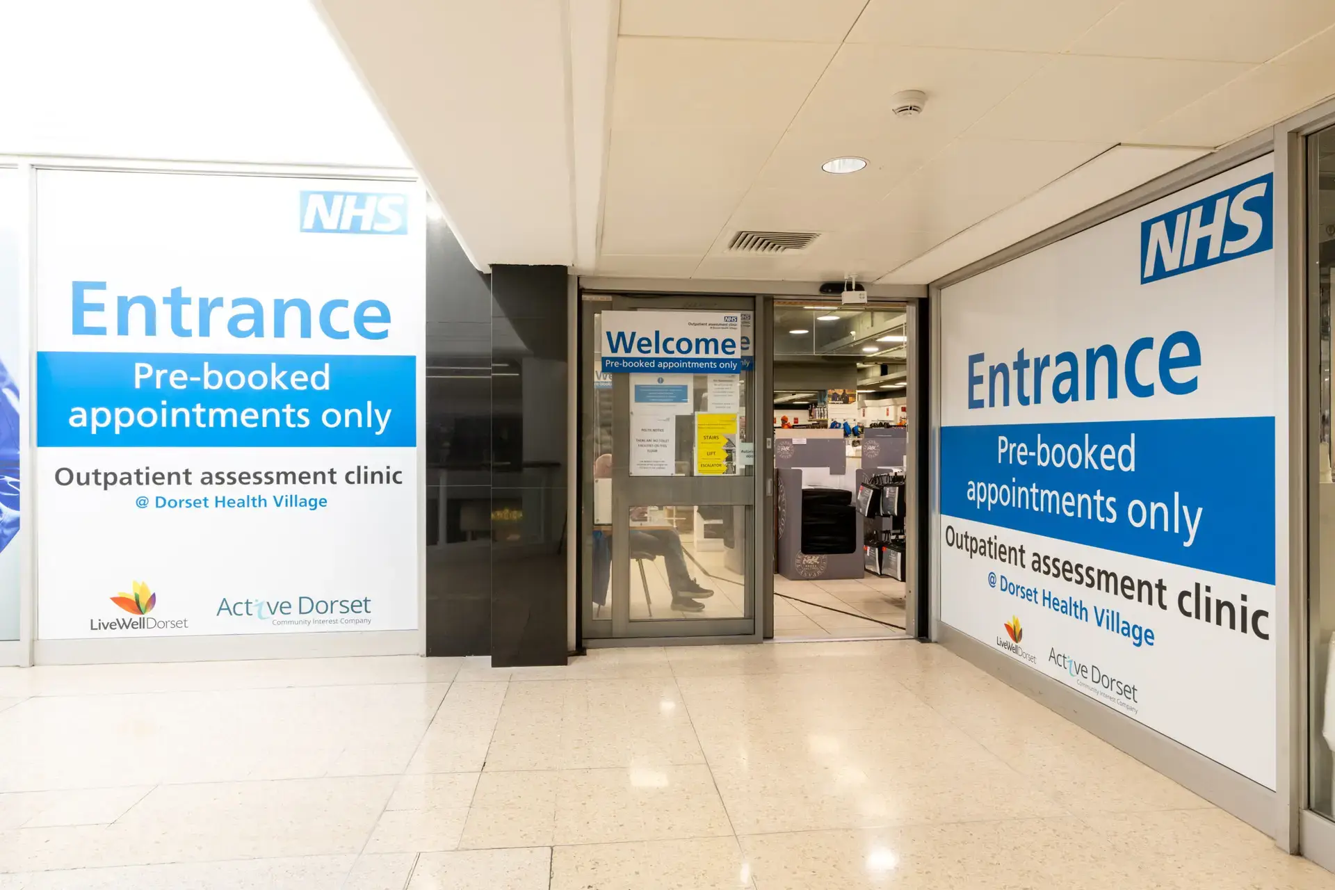 Exterior of the NHS Outpatient Assessment Clinic on the first floor of The Dolphin shopping centre. Large signs read: Entrance, Pre-booked appointments only, Outpatient assessment clinic at Dorset Health Village