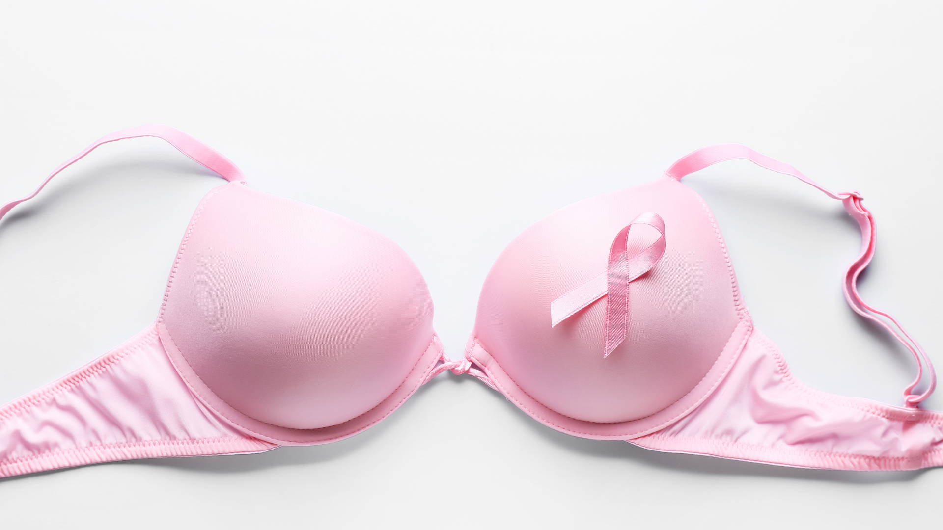 Pink bra laid flat on a white background. A pink breast cancer ribbon embellishes one side of the bra