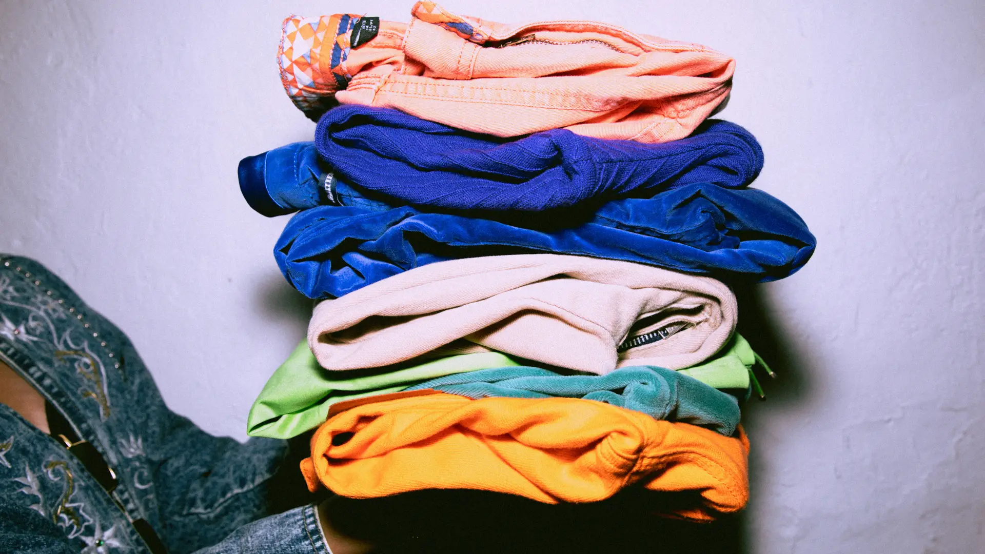 A woman in a demin jacket holds a stacked of folded colourful clothing